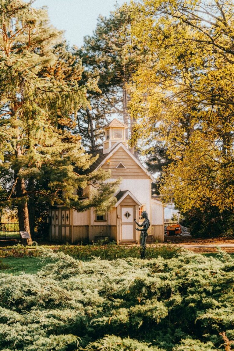 Small white building surrounded by trees and greenery.